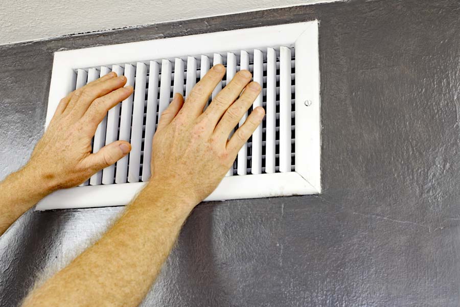 A pair of adult male hands feeling the flow of air coming out of an air vent on a wall near a ceiling. Man with hands in front of an air vent feeling for air flow.