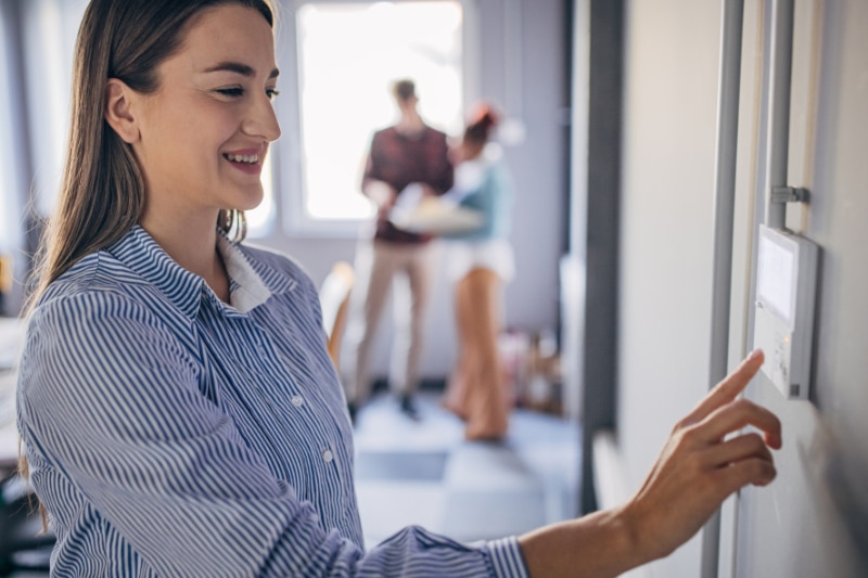 Commercial Thermostats and Controls. Young woman changing temperature on thermometer in the office.