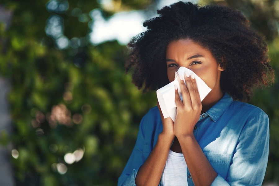 Woman blowing her nose outside due to seasonal allergies