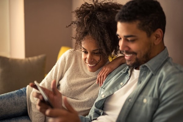 African american couple going over their heating bill on a tablet. How to save money on your heating bill this winter.|Sealing weather window tape on a wooden frame and home related objects placed on the window sill. How to save money on heat this winter.