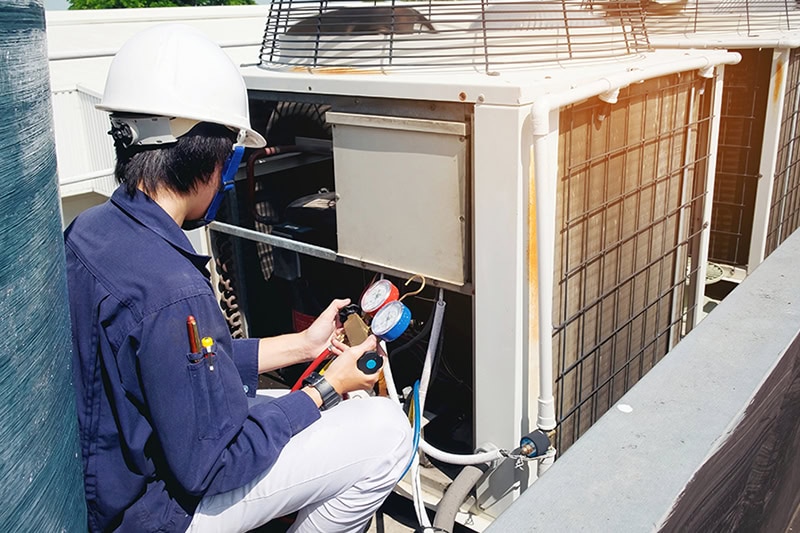 What To Do if Your Commercial AC System Breaks Down in Summer. A technician working on a commercial AC unit.