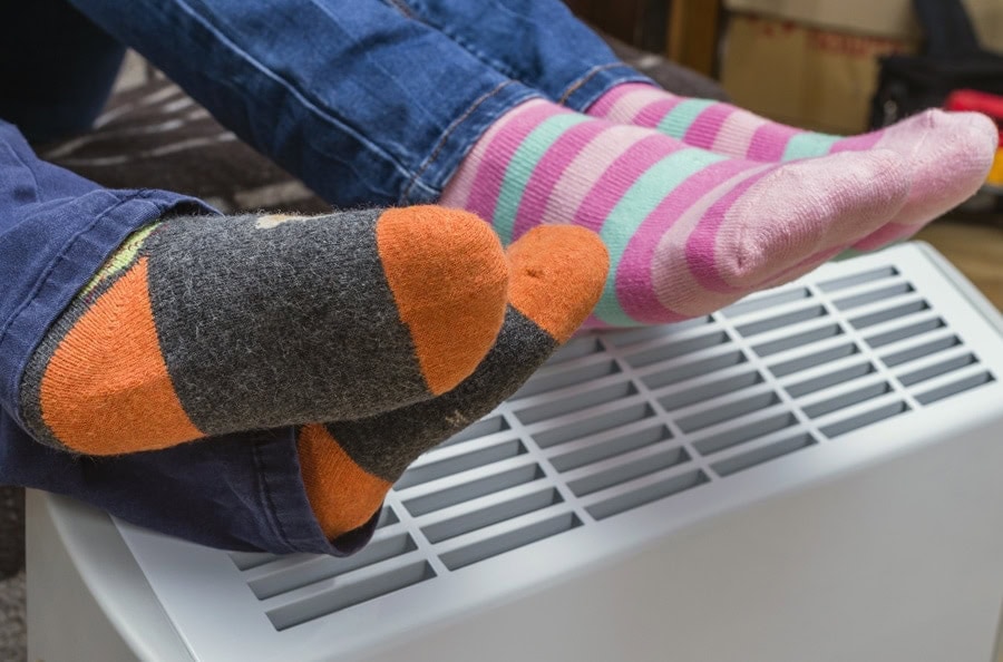 Homeowners relaxing and staying warm with their feet on their air ducts after following the furnace maintenance tips.