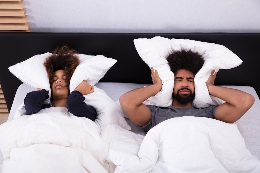 Elevated View Of Young Couple Lying In Bed Covering Their Ears With Pillow